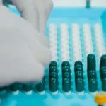 Tangan berglove menyusun kapsul obat di atas nampan steril dalam proses produksi farmasi sesuai standar GMP